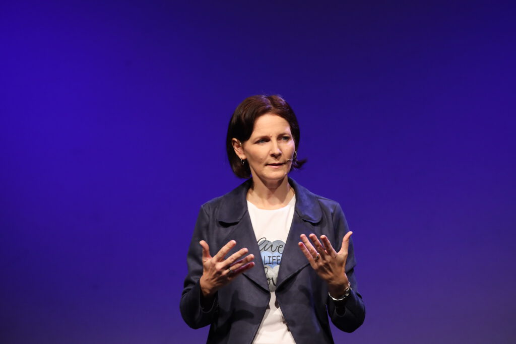 Kirsten Wunderle im Gespräch mit dem Publikum vor lila Hintergrund