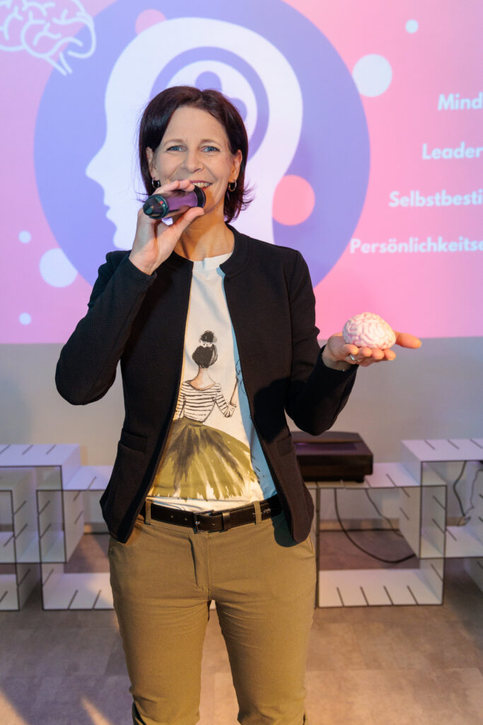 Kirsten Wunderle mit Mikrofon und einem Gehirn-Modell in der Hand