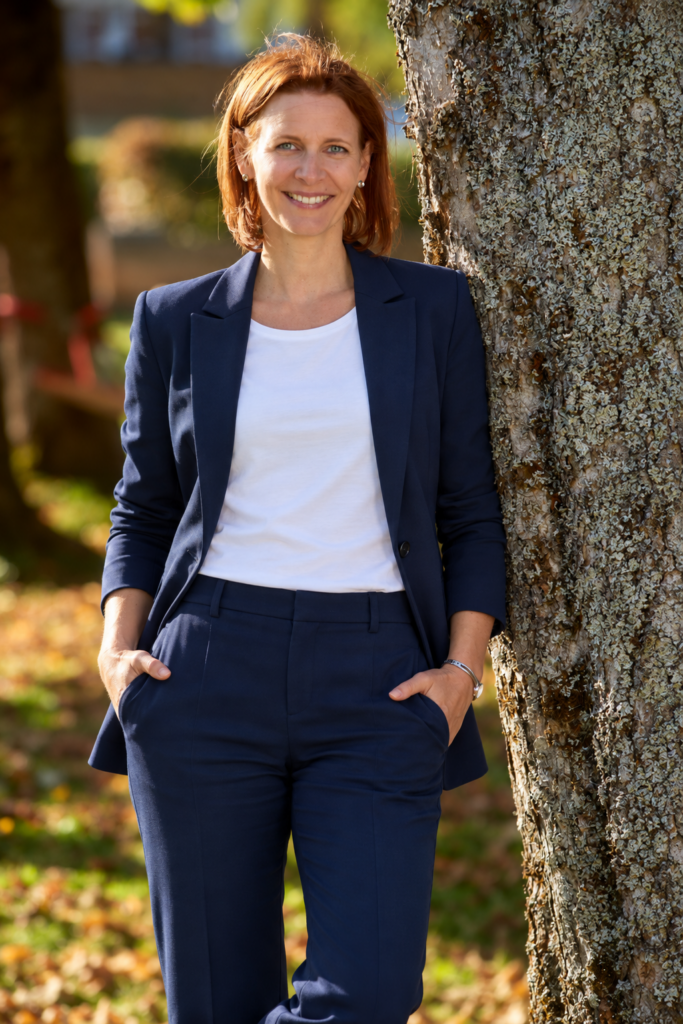Kirsten Wunderle im dunkelblauen Hosenanzug, an einen Baum gelehnt