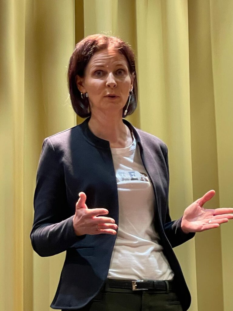 Kirsten Wunderle erklärt etwas vor einem goldenen Bühnenvorhang